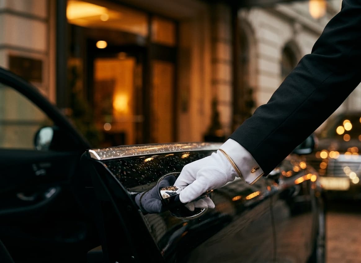 Chauffeur in white-gloved hand opening the rear door of a black Mercedes S-Class at night